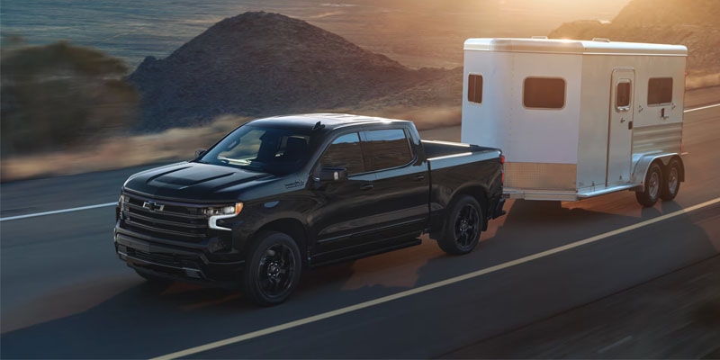 Pickup truck towing a travel trailer on a highway during sunset with mountains in the background, showing motion and outdoor travel scenery.