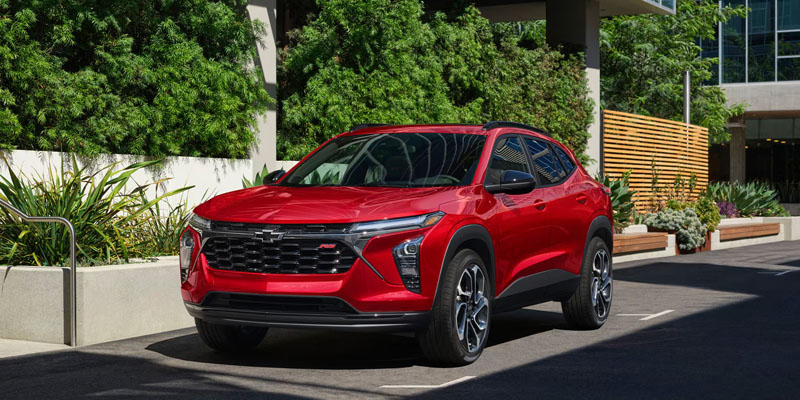 Red SUV parked on a quiet city street in front of modern buildings and greenery, showcasing a sleek exterior design.