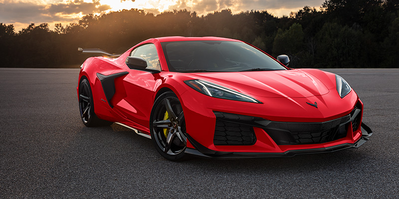 Red Chevrolet Corvette sports car parked on an open road at sunset, showcasing a low aerodynamic design and performance styling.